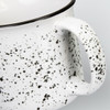 A ceramic mug with a speckled white design and a black rim, featuring a sturdy handle.