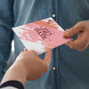 A5 greeting card in pink and white with a brushstroke design, held by one person and being handed to another.
