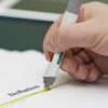 A hand holding a grey and green Tetra highlighter pen, marking yellow text on a white page.