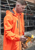 A man wearing an orange unisex packable rain jacket, focused on using a power tool on a construction site.