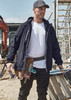 A man wearing a black unisex lightweight packable rain jacket, standing at a construction site with tools and equipment around.