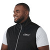A black men's softshell vest with a high collar and a logo on the front, worn over a grey shirt.