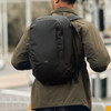 A backpack in black being worn by a person, showcasing a sleek design with a prominent logo on the back.