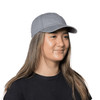 A grey organic washed cotton cap with a curved brim, worn by a woman with long hair. The cap includes a logo.