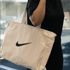 A large cream tote bag with a black logo being held by a person.