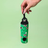 A green neoprene golf ball sleeve featuring a quirky pattern with golf flags and holes, held by a hand.