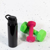 A drink bottle in black with a free flow lid, placed next to pink and green dumbbells on a speckled surface.