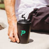 A travel cup in matte black with a green logo, featuring a secure lid and hand-held against a light background.