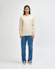 A model wearing a beige long-sleeve T-shirt with a pocket paired with olive green pants and casual sneakers.