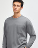 A model wearing a grey long-sleeve t-shirt with a pocket and a logo on the chest.
