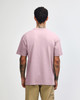 A person facing away wears a purple American Apparel Super Heavyweight T-Shirt, showing its back. The shirt has a subtle brand logo.