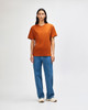 A model wearing an orange heavyweight t-shirt paired with olive green cargo pants and white sneakers, standing against a plain background.