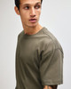 A model wearing an olive green American Apparel Super Heavyweight T-Shirt, featuring a simple design and crew neck.
