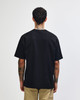A black American Apparel Super Heavyweight T-Shirt viewed from the back, paired with olive green trousers.