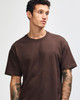 A brown super heavyweight t-shirt on a model with tattoos, featuring a plain design and a logo on the garment.