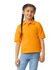 An orange Gildan youth polo shirt displayed on a girl with braided hair, smiling against a white background.