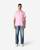 A man stands wearing a pink Gildan Light Cotton T-Shirt and light blue jeans, with minimal background detail.