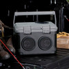 A grey and black sound box with a handle, featuring two speakers on the front, set on a vehicle's tray.