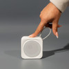 A portable white Bluetooth speaker with a textured speaker grille and a hand reaching towards it.