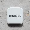 A compact mirror in a white case with a logo on the top, set against a textured stone background.