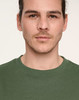 A close-up of a person wearing a green unisex crew neck sweater with a logo on the chest.