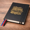 A black diary featuring a decorative gold design and multiple ribbon bookmarks in red, white, and blue.