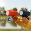 A red and blue bubble gun held by a child, with bubbles floating in the air and a scenic background.