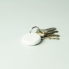 A white dual system item tracker sits alongside a set of metal keys on a light background. The tracker has a keyring attached.