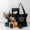 A black tote bag with a logo, surrounded by various sweet treat boxes, a candle, and decorative dried flowers.