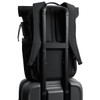 A black rolltop backpack is secured on a black suitcase, featuring padded straps and a side pocket.