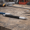 A black and silver precision pen lies on a workbench, surrounded by tools and small metal parts.