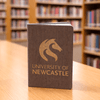 A brown eco notebook with a logo on the cover, placed on a wooden table in a library setting.