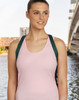 A woman in a pink tank top stands near water, wearing a bag with green straps and a logo.