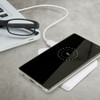 A white wireless charger with a smartphone displaying a charging symbol, next to glasses and a laptop.