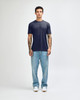 A model stands wearing a navy American Apparel Tri-Blend T-shirt and light blue jeans, with white shoes.