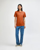 A model wearing an orange American Apparel Tri-Blend T-Shirt paired with blue jeans. The shirt has a logo.