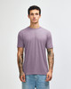 A man wearing a purple American Apparel tri-blend T-shirt paired with light blue jeans, featuring visible tattoos on his arms.