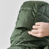 A close-up of a hand adjusting the hood of a green puffer jacket, featuring a logo on the back.