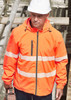 An orange packable rain jacket with reflective strips, worn by a person in a hard hat, standing near scaffolding.