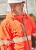 A bright orange unisex packable rain jacket with reflective stripes and a hood, worn by a man in a safety hat.