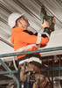 A unisex hi-vis full zip stretch taped hoodie in orange and black, worn by a worker using a drill on a scaffold.