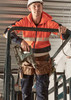 A unisex hi-vis full zip stretch taped hoodie in orange, worn by a person on a work platform, holding a power drill.