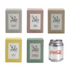 A set of six square candle boxes in various pastel colours: coconut milk and saffron, vanilla caramel, chocolate espresso, cinnamon and clove, eucalyptus and lemon myrtle. A Coca-Cola can is beside them.