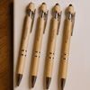 Four bamboo stylus pens with silver accents arranged on a light surface, each featuring a branding logo.