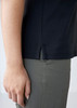 A side view of a navy women's polo shirt featuring a small slit at the hem, paired with light-coloured pants.