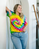A vibrant tie-dye adult T-shirt featuring a swirl of yellow, pink, blue, and green colours, paired with light blue jeans.