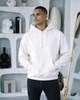 A white hoodie with a front pocket worn by a person against a stylish background with decorative objects.