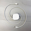 A retractable charging data cable in white, coiled with connectors at both ends, laid on a light wooden surface.