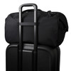 A black duffel bag sits on top of a black suitcase, featuring a trolley handle for easy transport.