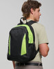 A black and neon green backpack is worn on the back of a young man, featuring mesh pockets and zippers.